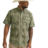 Front side view of green short sleeve pearl snap shirt that features a dark green desert print, double chest flap pockets, and shoulder yokes. 