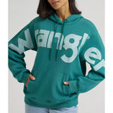 Close‑up of the turquoise Wrangler hoodie on a model, highlighting the bold Wrangler chest logo and kangaroo pocket.
