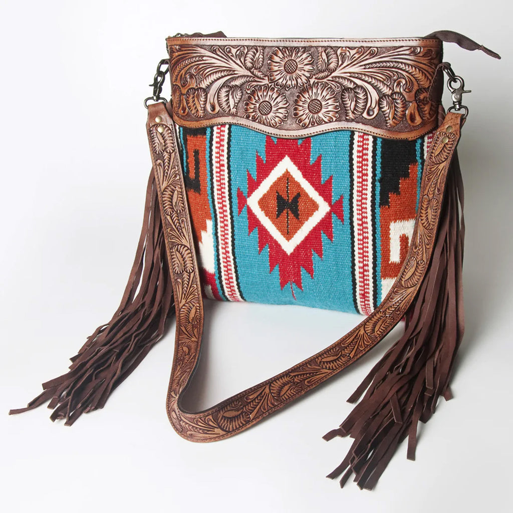 Wool blanket Bag with blue, red, orange, and black Aztec designs. Bag also features dark brown leather tooling on the top, shoulder strap, and fringe on the side. 