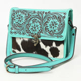 Turquoise tooled leather purse with the bottom half being black and white cowhide. Purse has a metal hook closure on the front and a long shoulder strap. 