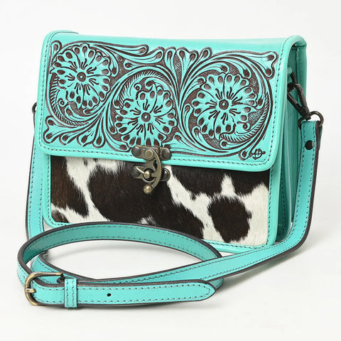 Turquoise tooled leather purse with the bottom half being black and white cowhide. Purse has a metal hook closure on the front and a long shoulder strap. 