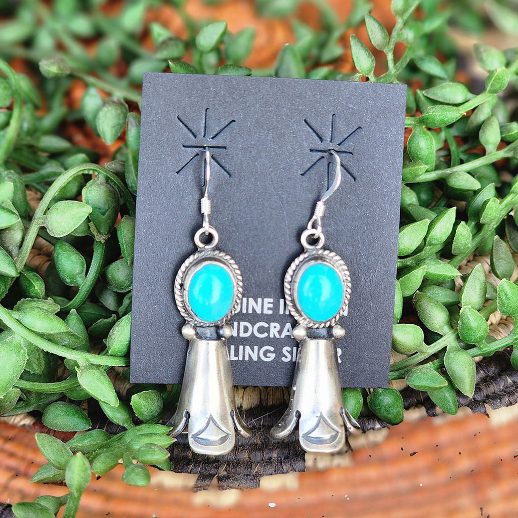 Turquoise and silver earrings on a branded card with green foliage in the background