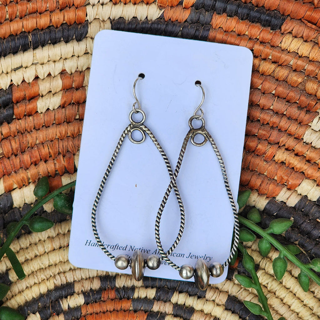 Pair of silver teardrop earrings with beads on a card, placed on a woven mat with natural colors.