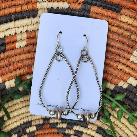 Pair of silver teardrop earrings with beads on a card, placed on a woven mat with natural colors.