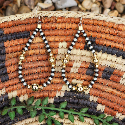 Pair of silver and gold beaded earrings on a woven surface with green leaves.