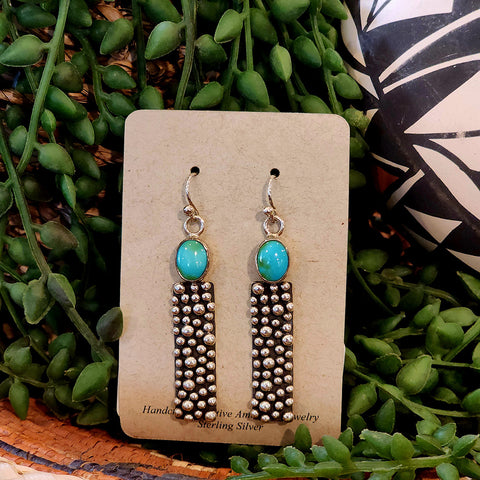 Pair of earrings on a card with green leaves in the background