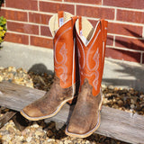 Pair of brown and orange cowboy boots on a wooden bench with a brick wall background.