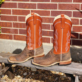 Pair of brown and orange cowboy boots on a wooden bench with a brick wall background.