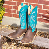 Pair of brown and turquoise cowboy boots on a wooden bench with a brick wall background.