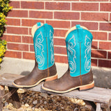 Pair of brown cowboy boots with turquoise tops on a wooden bench against a brick wall.