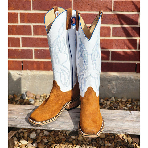 Pair of brown and white cowboy boots on a wooden bench with a brick wall background.