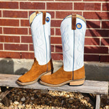 Pair of white cowboy boots with brown accents on a wooden bench against a brick wall.