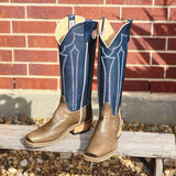 Pair of blue and grey cowboy boots on a wooden bench with a brick wall background.