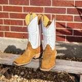 Pair of tan and white cowboy boots on a wooden bench with a brick wall background