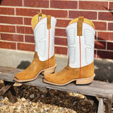 Pair of tan cowboy boots with white tops on a wooden bench against a brick wall.