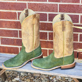 Green carpincho boots with brown top in front of brick wall.