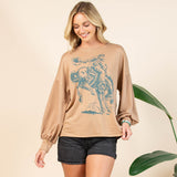 Female model wearing a mocha long sleeve shirt featuring a turquoise bronc rider graphic, shown to highlight the Western design, fit, and sleeve detail.