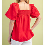 Back view of a model in the red smocked puff sleeve blouse, highlighting the clean back line, gathered smocking, and flattering, feminine fit.