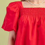 Close‑up of a model wearing the red smocked puff sleeve blouse, showing the textured smocked bodice, soft fabric detail, and feminine sleeve design.