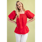 Model wearing the red smocked puff sleeve blouse, front view showing the fitted smocked bodice, playful puff sleeves, and flattering feminine silhouette