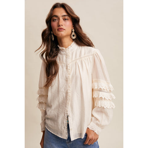 Model wearing the Cream Lace Ruffle Sleeve Pintuck Blouse in a front view, showing the lace details, tiered ruffle sleeves, and soft pintuck texture.
