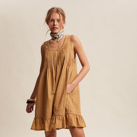 Model wearing the Textured Pleated Mini Dress in a front view, showing the textured fabric, pocket and pom pom accents