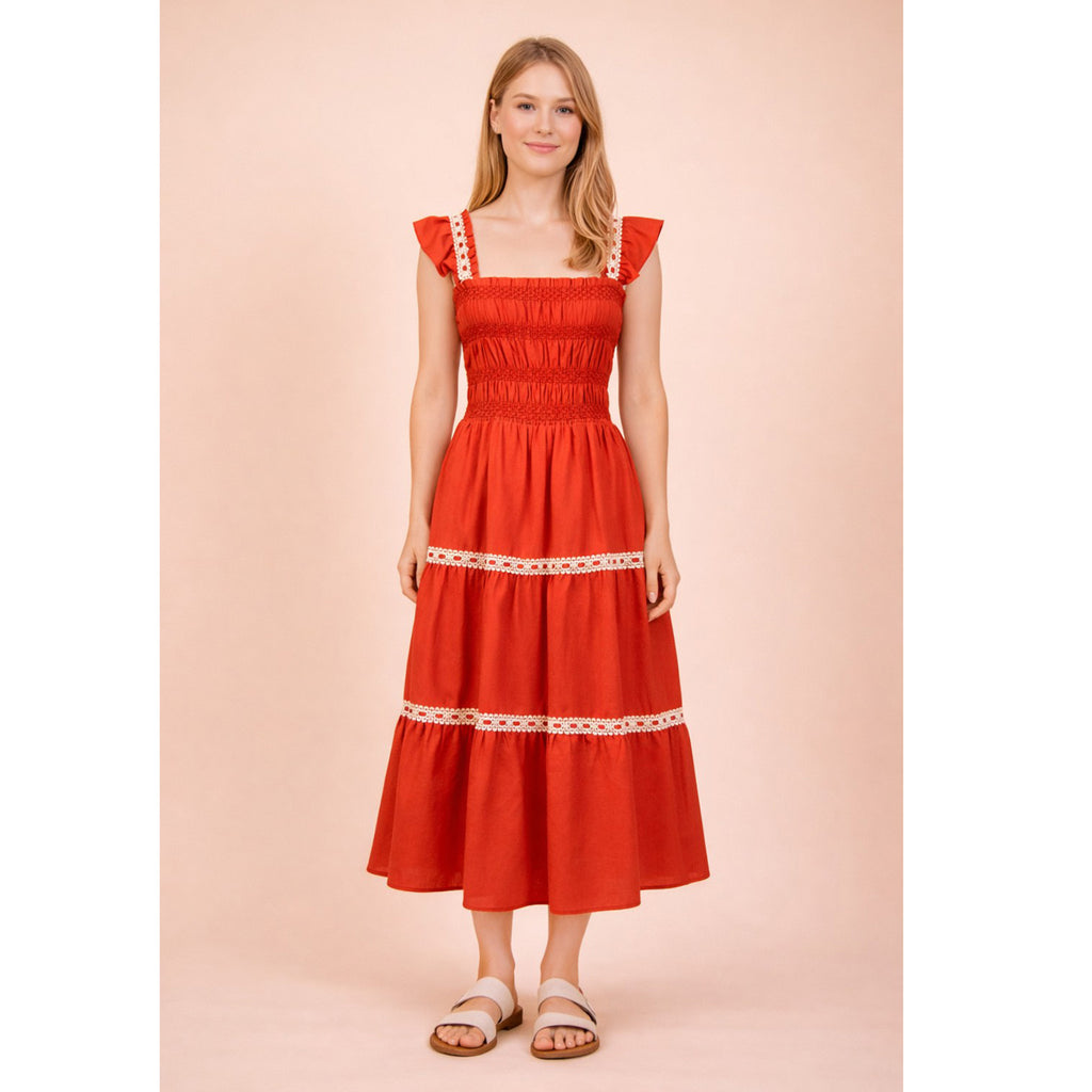 Model wearing the red smocked ruffle‑strap tiered midi dress in a front view, showing the softly smocked bodice, ruffle straps, and flowing tiered skirt with cream ribbon trim.