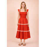 Model wearing the red smocked ruffle‑strap tiered midi dress in a front view, showing the softly smocked bodice, ruffle straps, and flowing tiered skirt with cream ribbon trim.