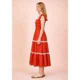 Side view of the model in the red smocked ruffle‑strap tiered midi dress