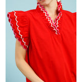 Close‑up of model wearing a solid red scallop trim ruffle sleeve top focusing on the scalloped trim and ruffle sleeve detail.