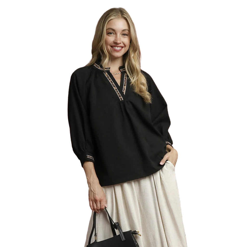 Woman wearing a solid black 3/4 length shirt featuring a brown cheetah print collar and sleeve detail