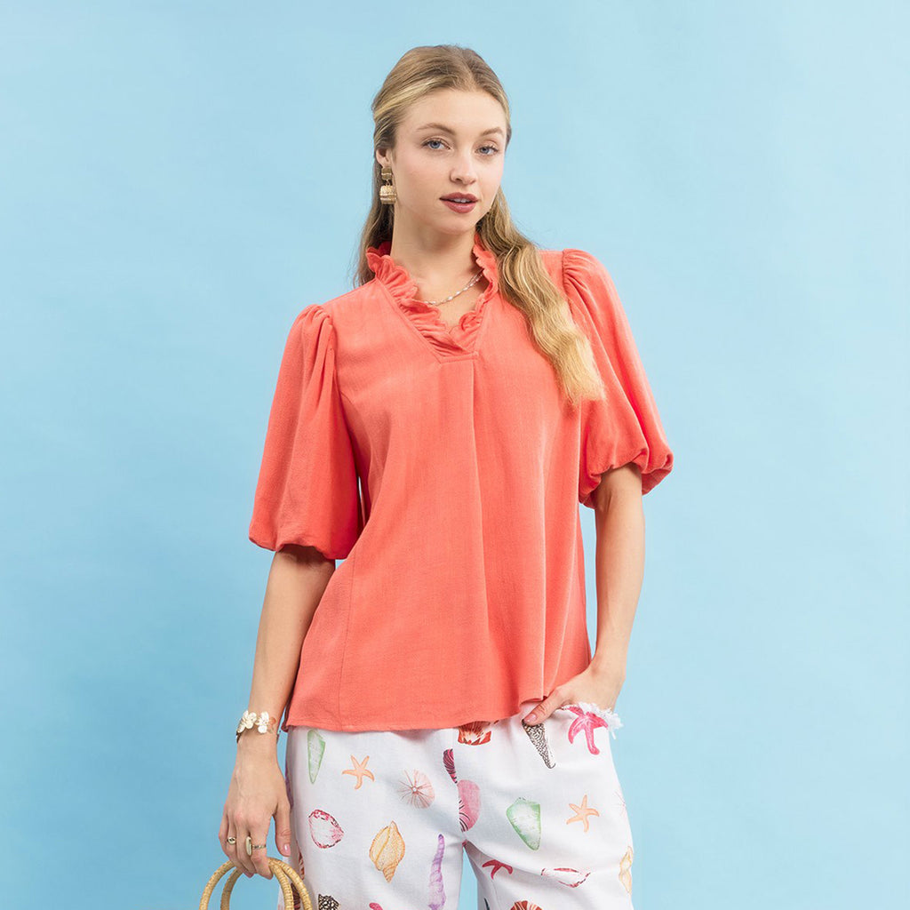 Model wearing a coral linen scallop V‑neck puff sleeve top, front view showing the scalloped neckline, puff sleeves, and lightweight linen texture.