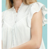 Close‑up of model wearing an off‑white smocked yoke ruffle sleeve blouse focusing on the smocked yoke texture and delicate ruffle sleeve detail.