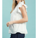 Side view of model in an off‑white smocked yoke ruffle sleeve blouse highlighting the fluttery ruffle sleeves and relaxed drape.