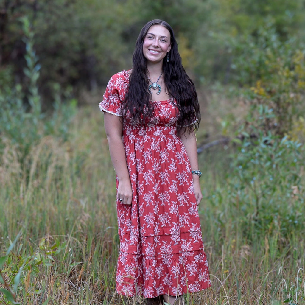 Model wearing the Rust Scarlet Meadow Dress, front view showing the flowing silhouette, warm rust tones, and relaxed Western‑inspired fit.