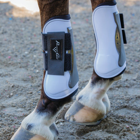 Close up of horse wearing white protective boots standing on sandy ground.