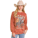Woman wearing a rust distressed sweatshirt with graphic design cowboy on a bronc