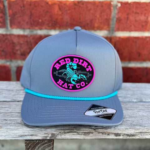 Grey cap with turquoise rope and pink and turquoise red dirt scorpion logo.