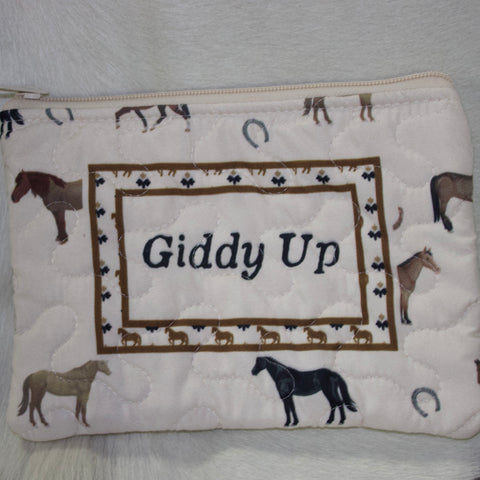 Small white makeup bag with a variety of horse designs, "Giddy Up" written in the middle and a floral border surrounding it. 