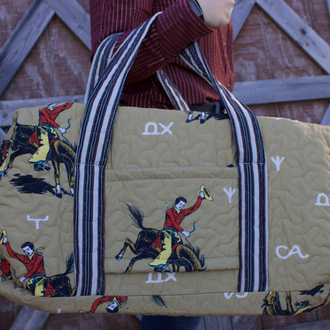 Gold Quilted duffle bag with retro cowboy graphics and blue and red striped straps. 