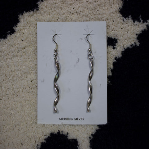 Long sterling silver earrings that are flat, hang vertically and are in a twisted swirl design.