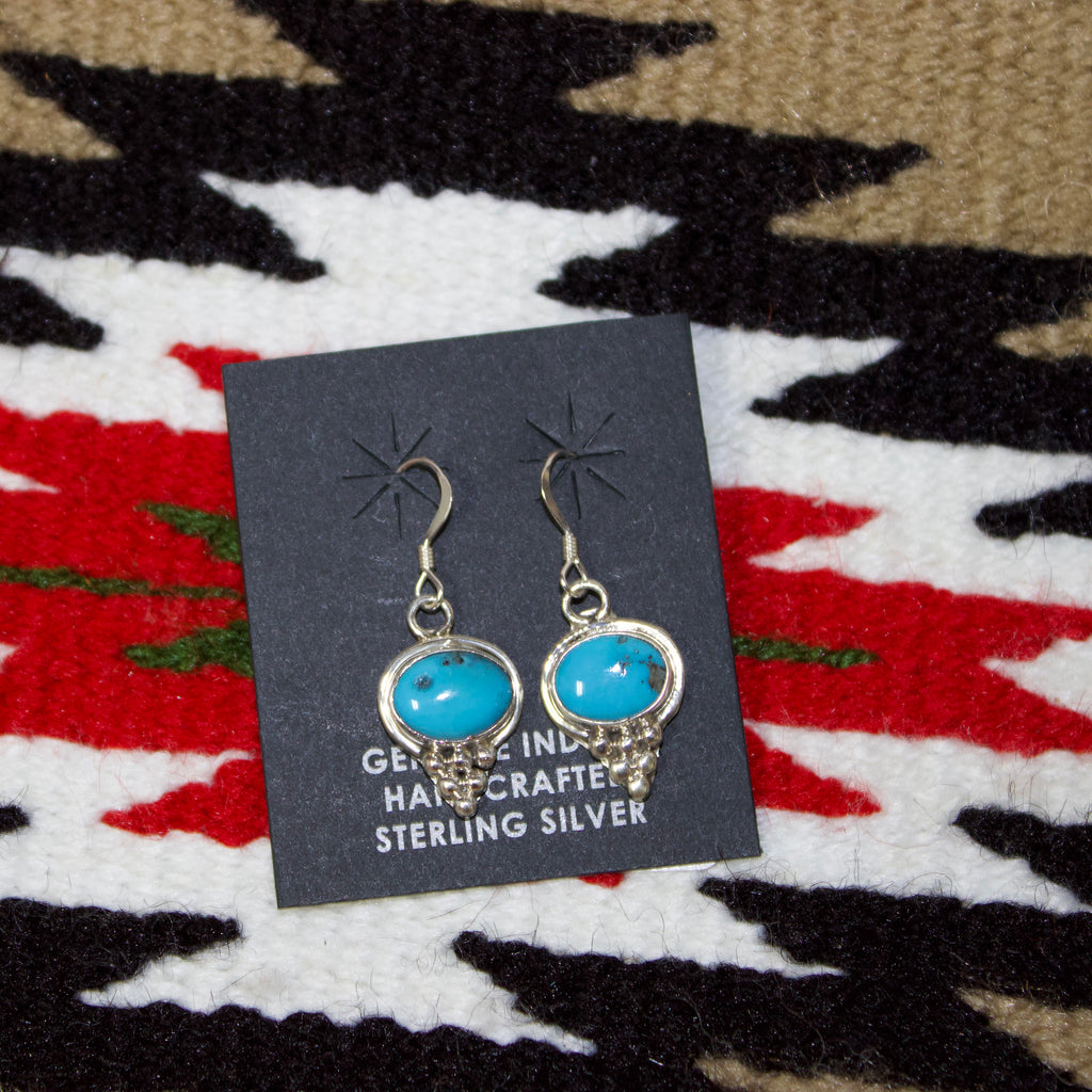 Sterling silver earrings with horizontal oval shaped Kingman turquoise stones in the middle and a diamond shaped silver accent on the bottom. 