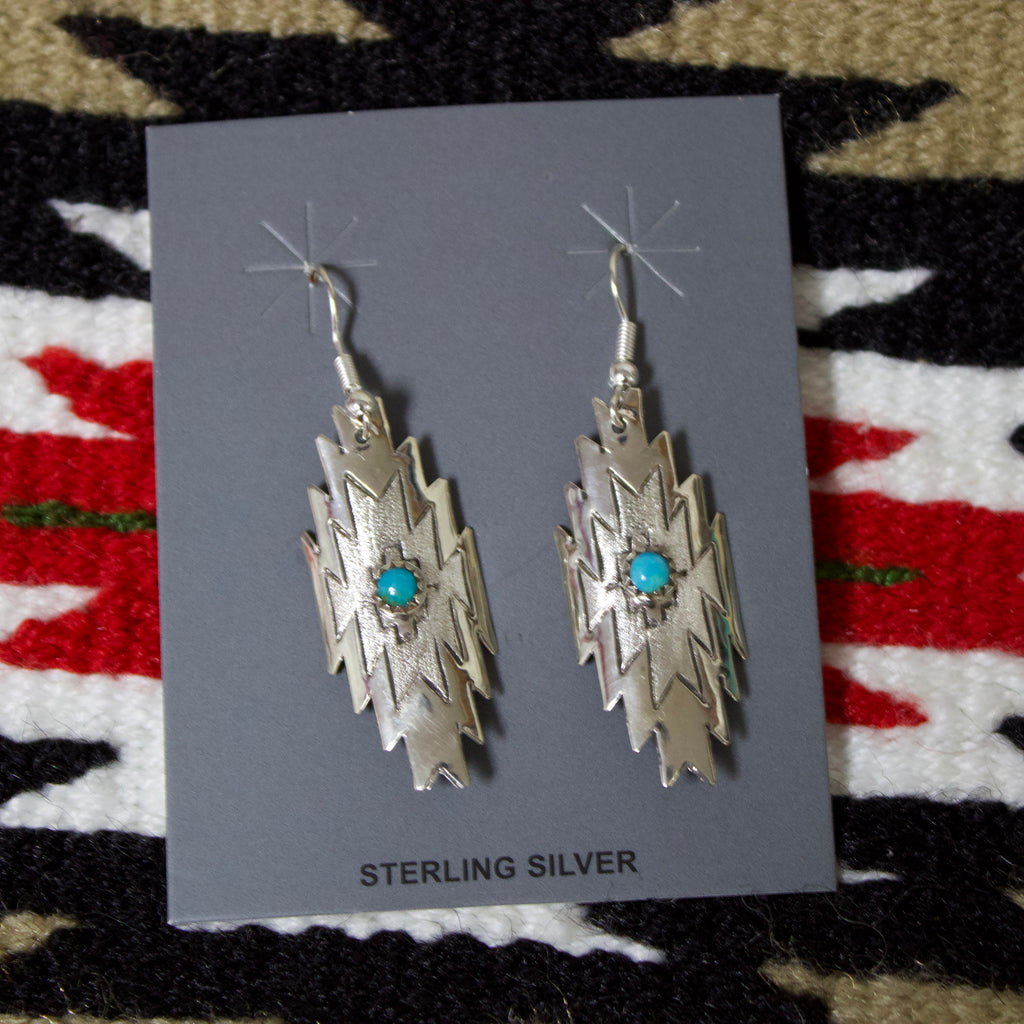 Sterling silver earrings in the shape of an Aztec design and a small turquoise stone in the middle. 