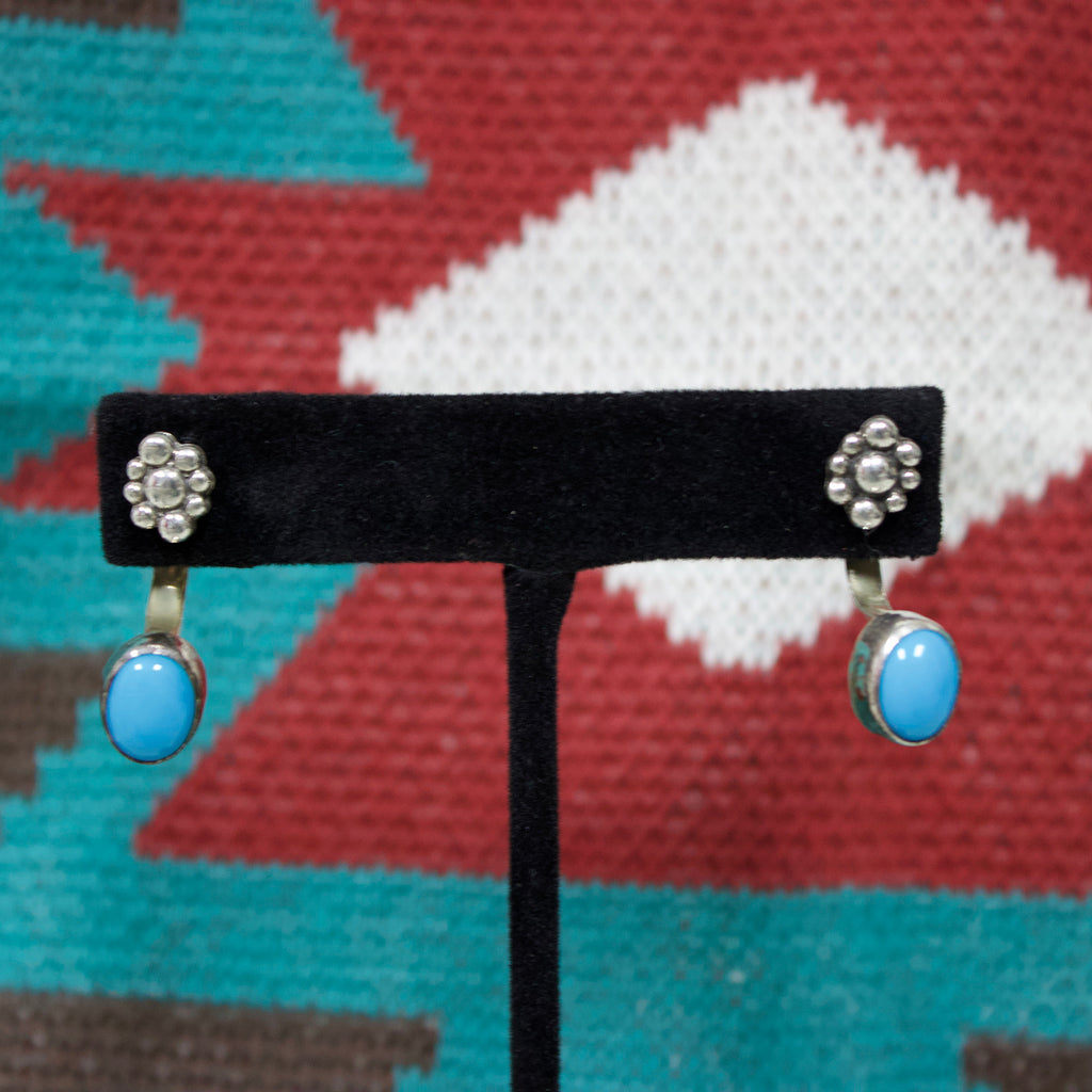Sterling silver earrings that have a silver flower stud in the front and a turquoise stone that hooks around the bottom from the back. 