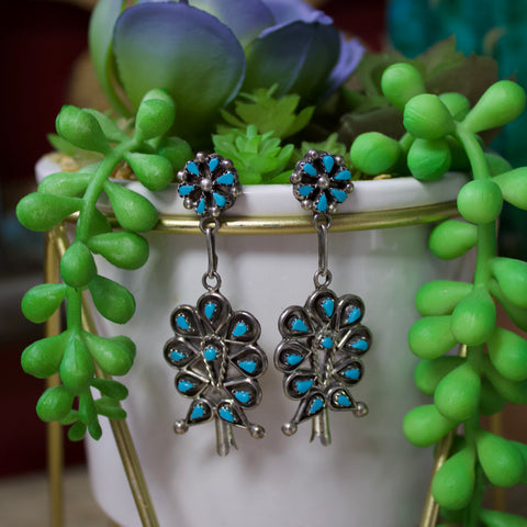 Set of earrings hanging off of a flower pot. Earrings are a Zuni Blossom design and are silver with Kingman turquoise stones. 