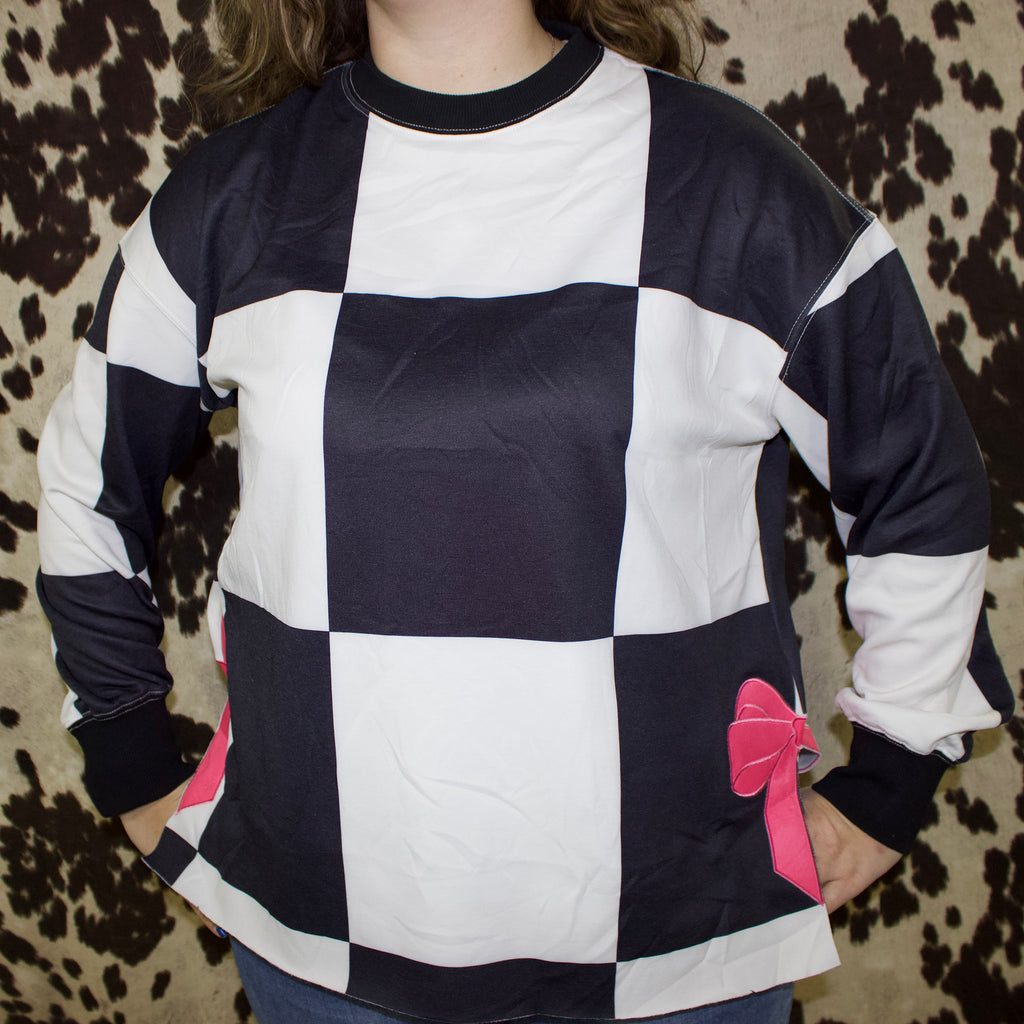 Model is facing front wearing a black and white large checkered long sleeve crew neck. 