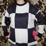 Model is facing front wearing a black and white large checkered long sleeve crew neck. 