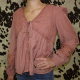 Front of the shirt, it is a mauve long sleeve shirt with floral lace detailing on the top and around the forearm. It has a v neckline, a string to tie in the front, and buttons that go down.