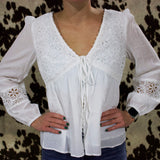 Front of the shirt, it is a white sheer long sleeve shirt with floral lace detailing on the top and around the forearm. It has a v neckline, a string to tie in the front, and buttons that go down.