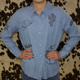 Light wash denim long sleeve shirt with western themed embroidery and white pearl snaps.